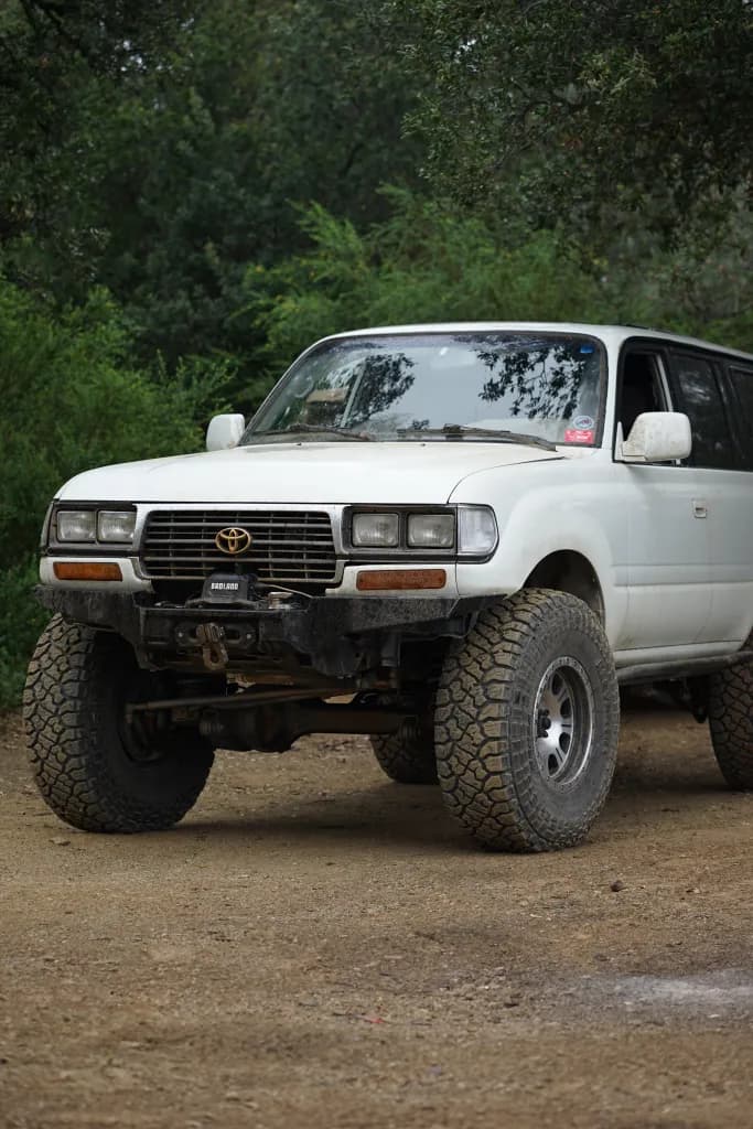 Lifted white Toyota Land Cruiser FZJ80 parked on a forest off-road trail